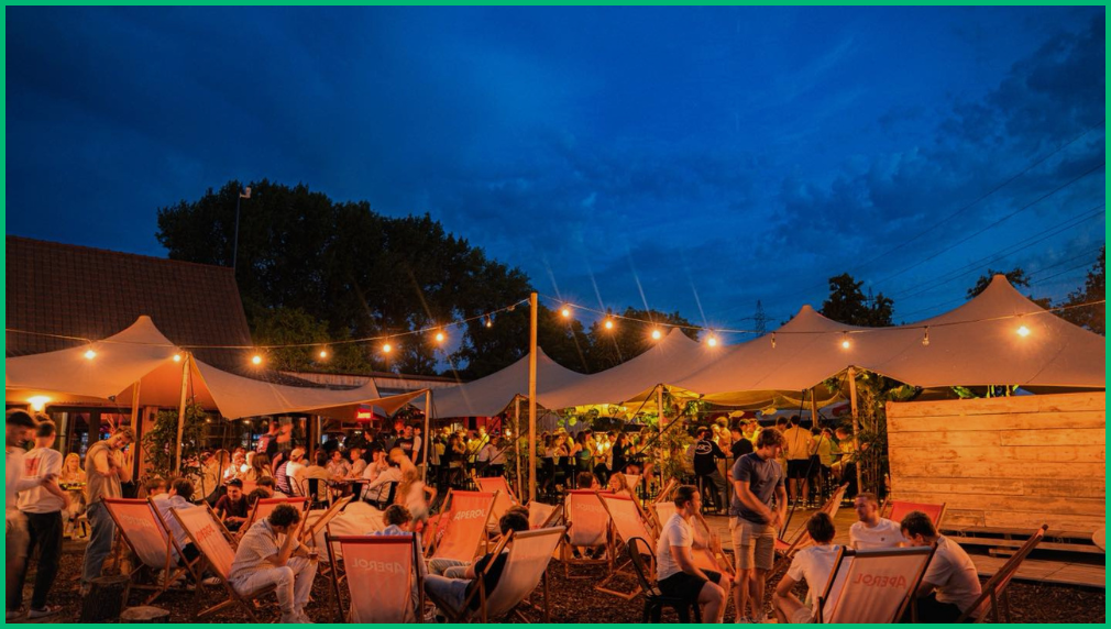 Avondsfeer bij zomerfestival met witte stretchtenten fairy lights en gasten zittend buiten bij schemering