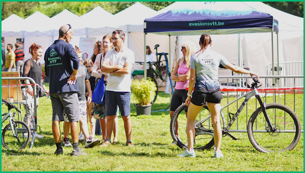 Branded vouwtent van mountainbike club Evasions VTT als standplaats op outdoor sportevenement met bezoekers en fietsen
