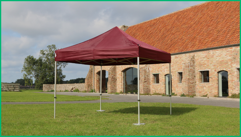Bordeauxrode vouwtent opgesteld voor een landelijke stenen boerderij op een grasveld