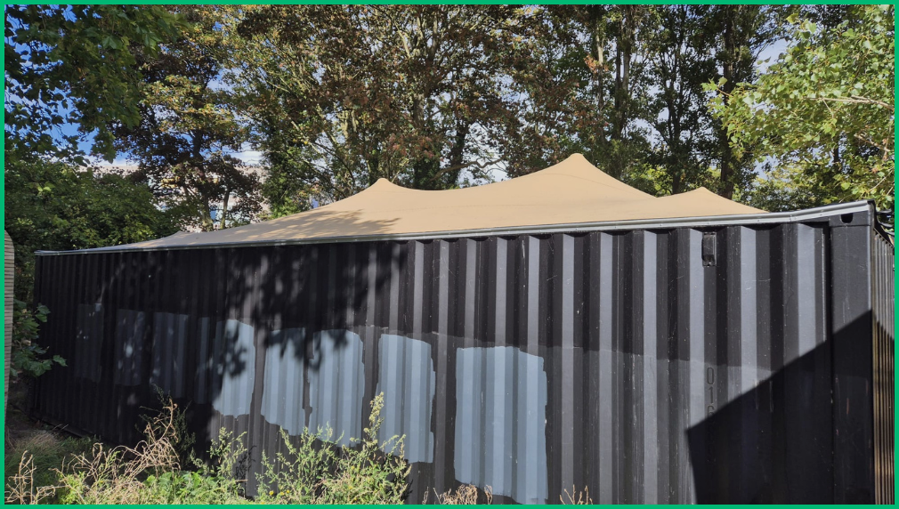 Beige stretchtent pieken boven zinken wand met bomen bij Les Cabanes Oostende kust