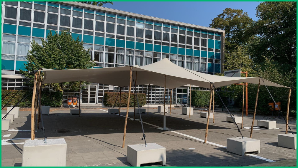 Beige stretchtent als schaduwstructuur in schoolplein voor moderne school met glazen gevel